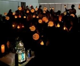 Group of educators holding lit lanterns in a darkened room. 